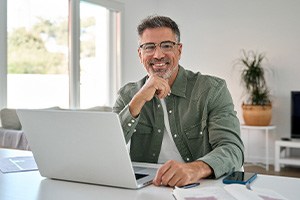 Man with glasses smiling while working on laptop