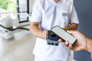 Hand holding out smartphone to device held by dentist to pay for services