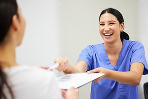 Dental staff in Michigan City smiling while offering forms to patient