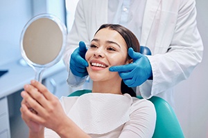 A woman admiring her smile with a hand mirror after her treatment