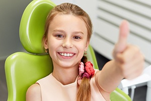 Young girl in dental chair giving thumbs up