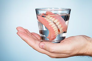 Hand holding glass of water with dentures