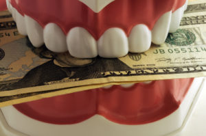 Model teeth biting down on twenty-dollar bills
