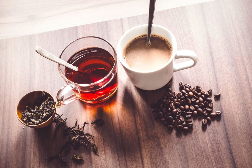 Bird's eye view of a tea leaves and coffee beans next to cups of tea and coffee